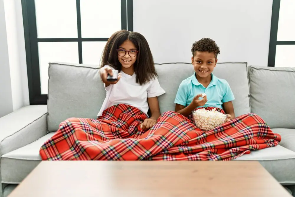 Two Black children under a blanket watching Black Disney movies