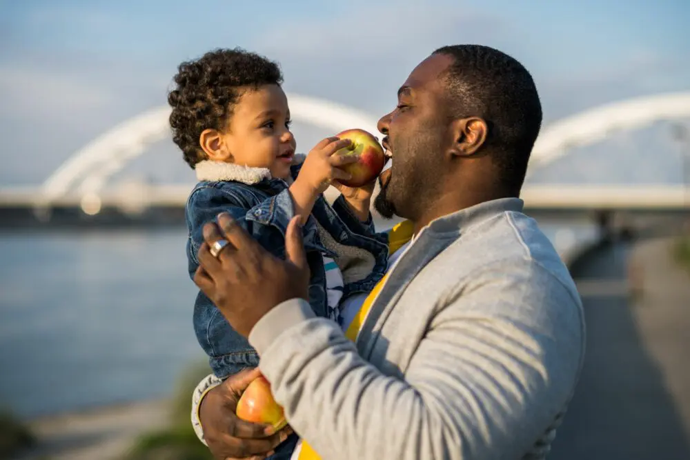 Black Father holding Black child with apples 